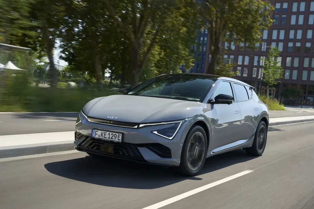 Grijze Kia EV6 rijdt op een boomrijke stadsweg.