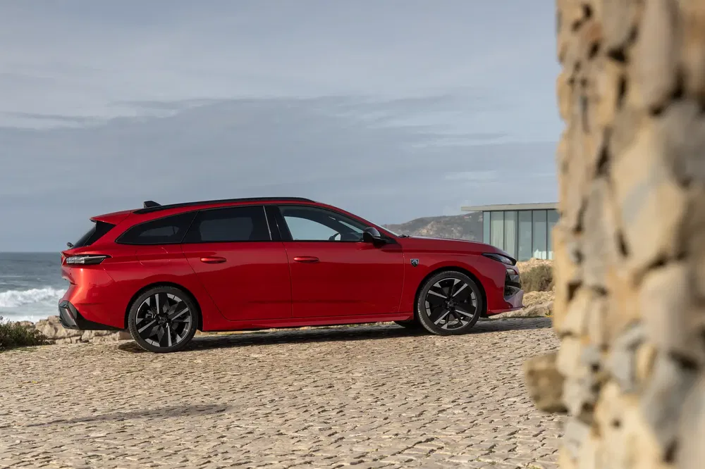 Rode Opel Astra stationwagen geparkeerd op een geplaveide weg met uitzicht op de oceaan.