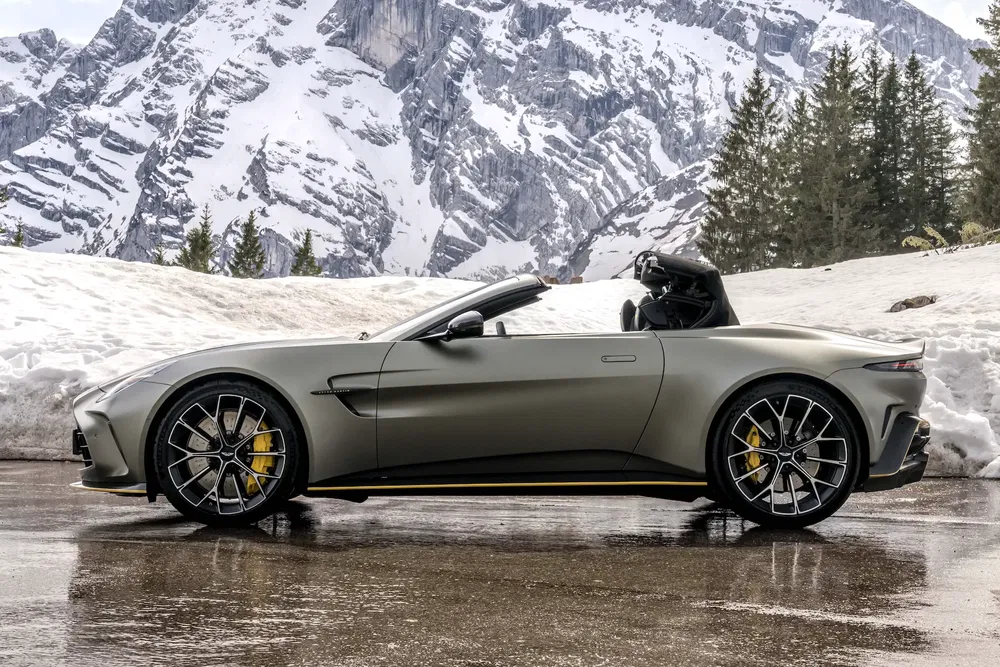 Voiture de sport Aston Martin cabriolet grise sur fond de montagnes enneigées.
