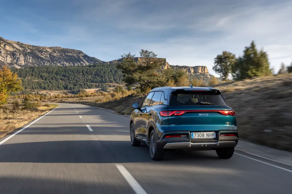 SUV BYD bleu sur route de campagne montagneuse, ciel clair et environnement naturel.