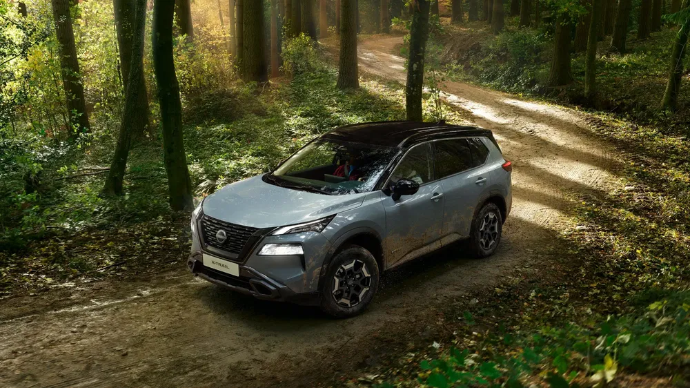 SUV Nissan X-Trail argent sur un chemin forestier lumineux.