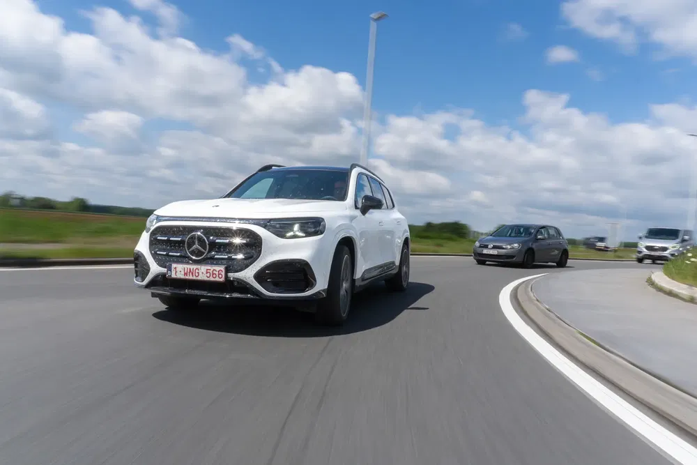 Mercedes-Benz GLB blanc sur route ronde, suivent plusieurs voitures dans un cadre rural.