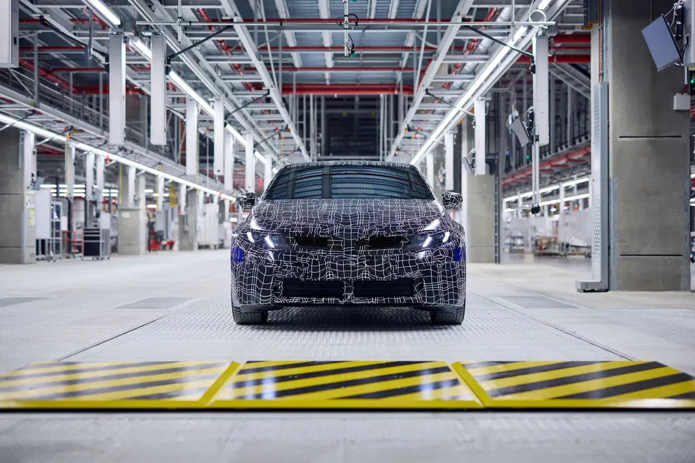 {"fr":"Voiture BMW camouflée dans une usine de fabrication moderne avec éclairage industriel.","nl":"Verborgen BMW-auto in moderne autofabriek met industrieel verlichtingssysteem."}