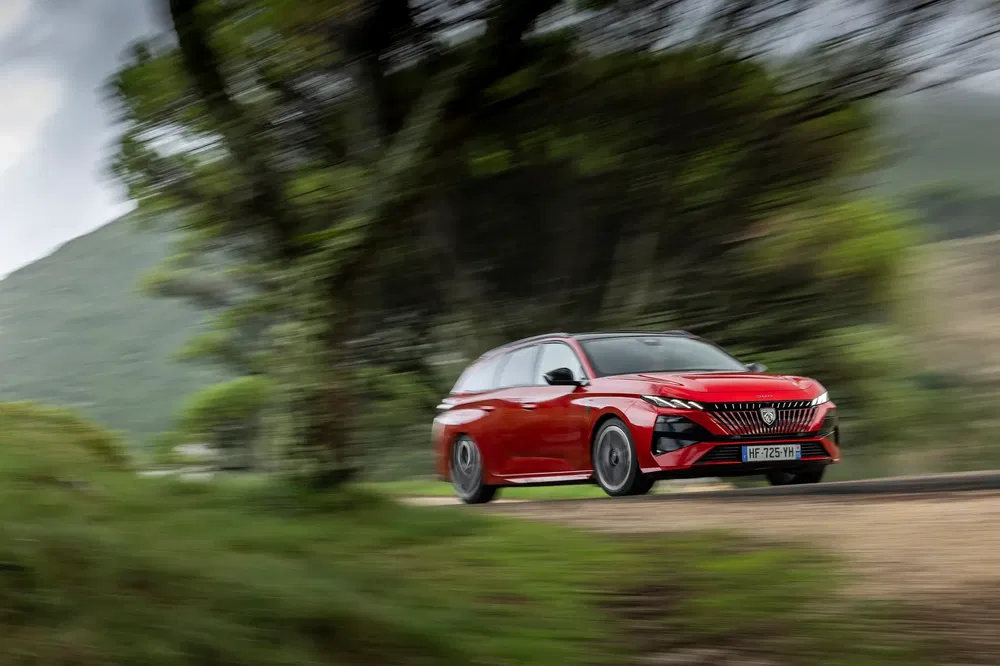 Peugeot 508 SW in rood, snel rijdend op een bochtige weg met bomen, dynamisch ontwerp.