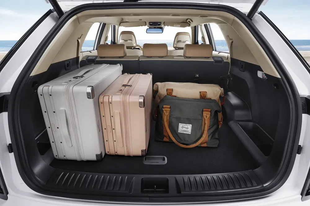 Ruime kofferbak van auto met drie koffers en reistas, strand op achtergrond.