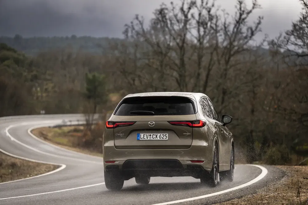 Mazda CX-60 roule sur une route sinueuse sous un ciel orageux et nuageux.