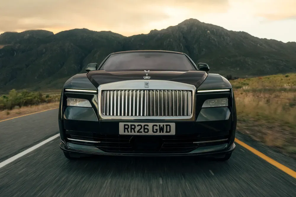 Rolls-Royce noire sur une route pittoresque, montagnes en arrière-plan, au coucher du soleil.