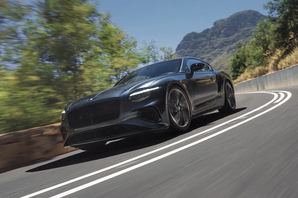 Bentley Continental GT noire sur une route sinueuse, montagnes en arrière-plan, temps ensoleillé.