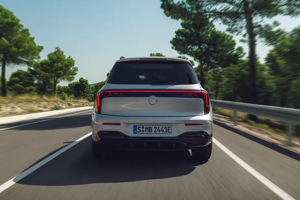 SUV Mercedes-Benz EQB électrique sur route forestière paisible, arrière élégant et moderne.
