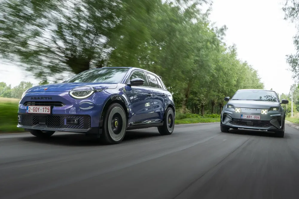 Twee blauwe en grijze elektrische Abarth-auto's rijden op een door bomen omzoomde weg.