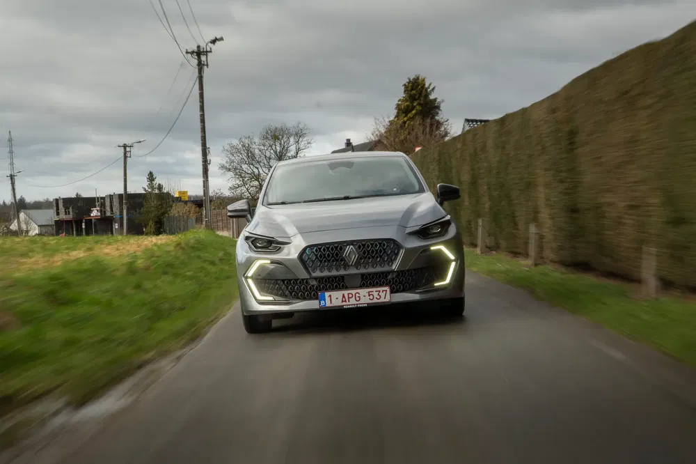 Grijze sportwagen op plattelandsweg met opvallende LED-koplampen aan.