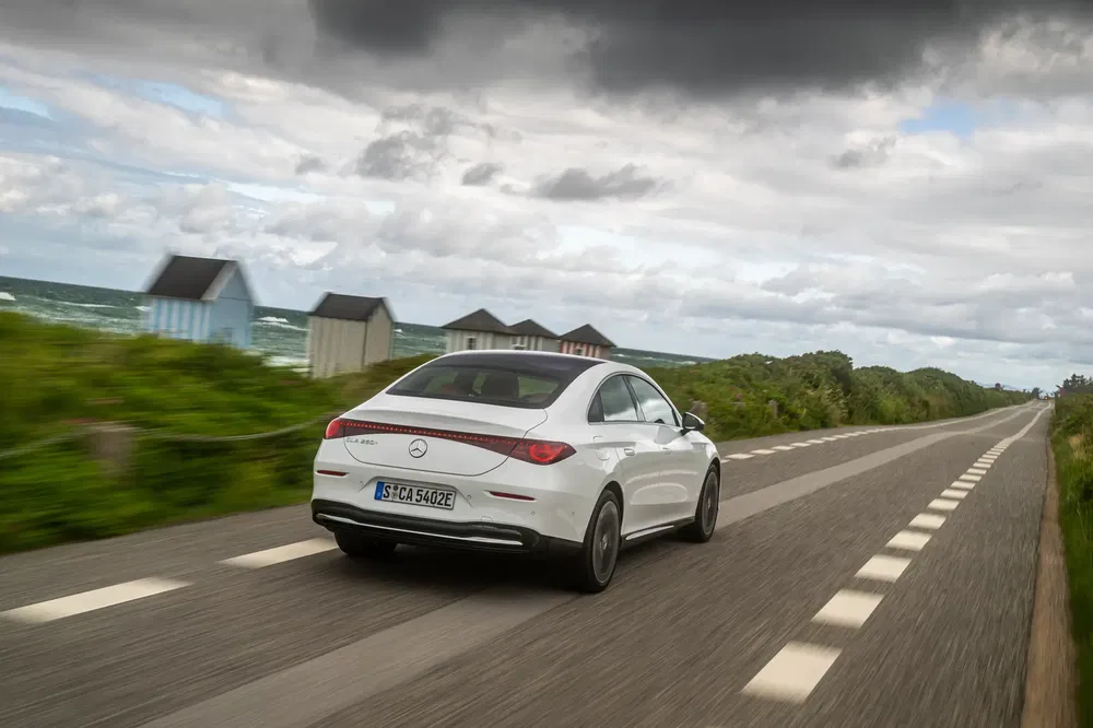 Witte Mercedes-Benz A250e rijdt langs schilderachtige kustweg onder bewolkte hemel.
