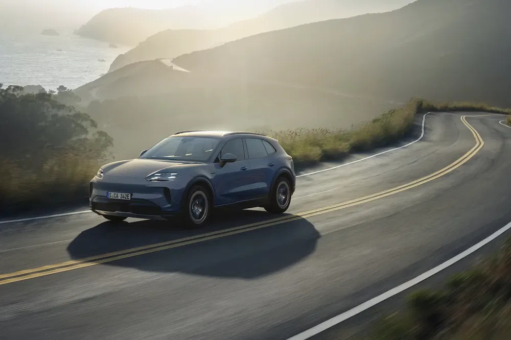 Porsche électrique sur une route côtière sinueuse au coucher du soleil, performance élégante.