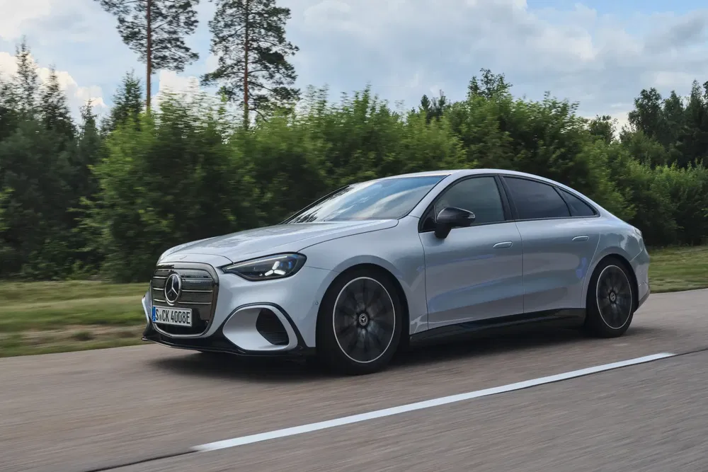Mercedes-Benz Classe E argentée roulant sur une route bordée d'arbres verts.