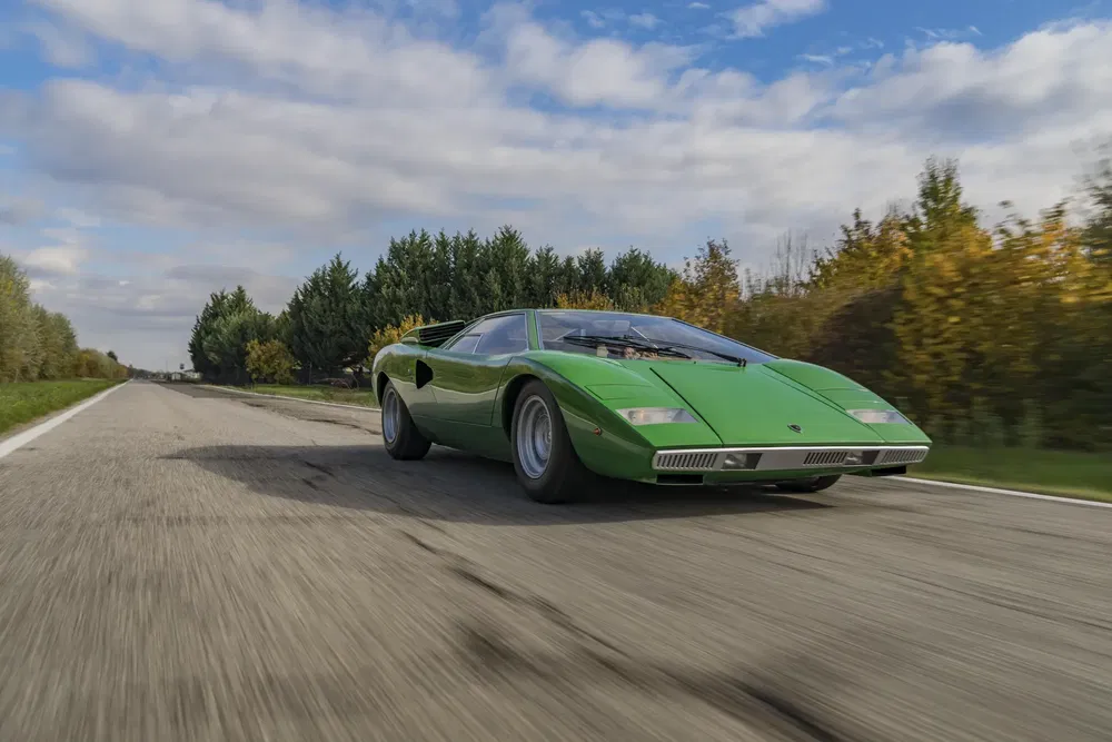 {"fr":"Lamborghini Countach verte classique sur une route de campagne, sous un ciel partiellement nuageux.","nl":"Klassieke groene Lamborghini Countach op een landelijke weg onder gedeeltelijk bewolkte hemel."}