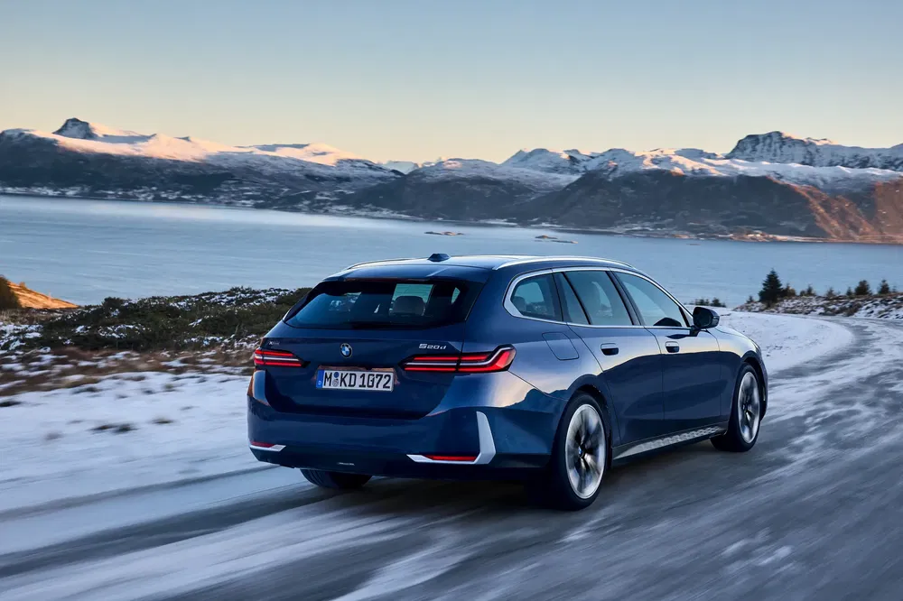 {"fr":"BMW Série 5 Touring roulant sur une route enneigée avec vue sur le lac et montagnes.","nl":"BMW 5 Serie Touring op besneeuwde weg met uitzicht op meer en bergen."}
