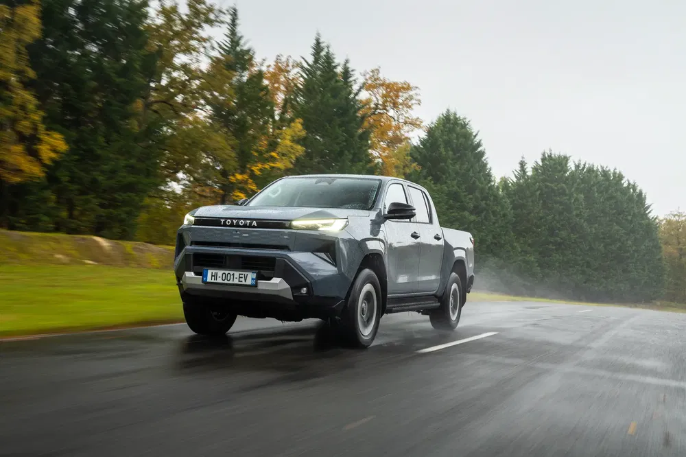 Toyota Hilux roulant sur route mouillée avec arbres en arrière-plan.