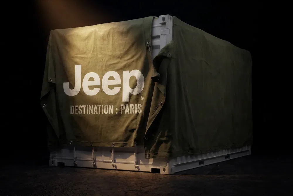 Caisse couverte Jeep avec inscription 'Destination Paris', éclairée dramatiquement dans un studio sombre.