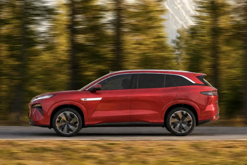 SUV rouge en mouvement sur route, arrière-plan flou d'arbres verts.
