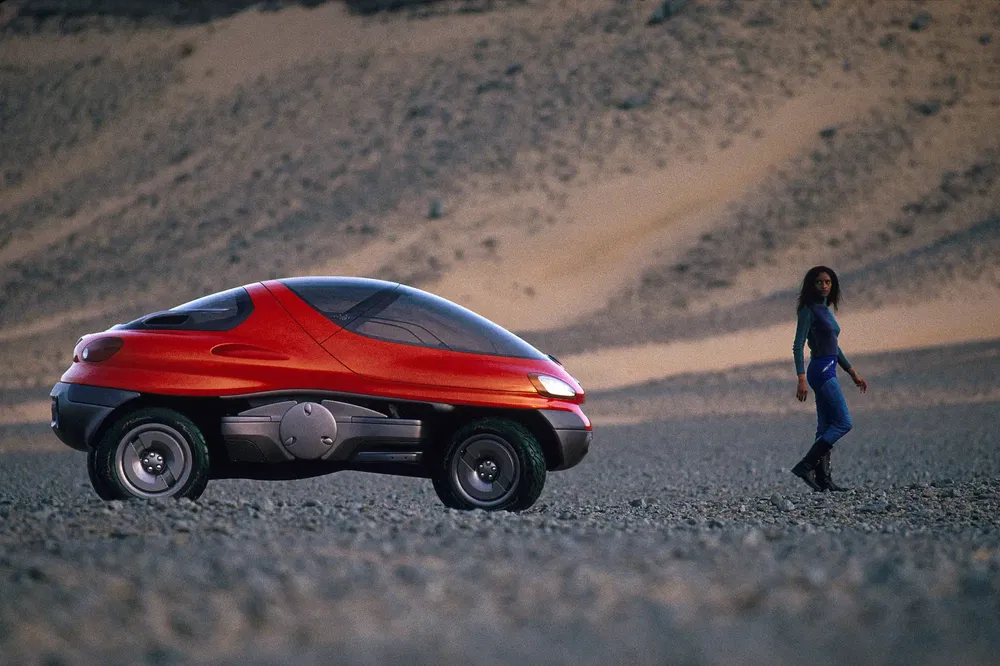 Rode Renault Racoon conceptauto in woestijn met een vrouw op de achtergrond.