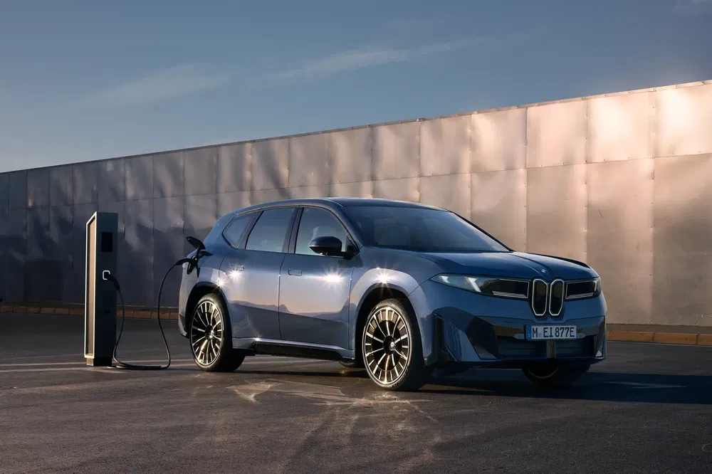 Moderne elektrische BMW laadt op bij laadstation in zacht avondlicht.