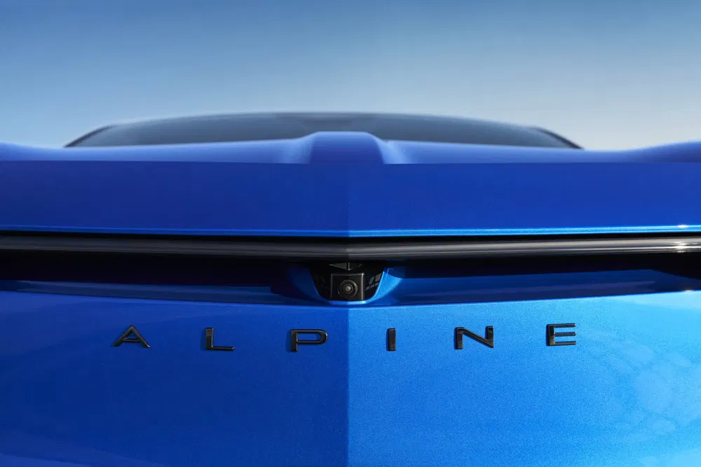 Achterdetail van een blauwe Alpine A110 met geïntegreerde camera, heldere lucht op de achtergrond.