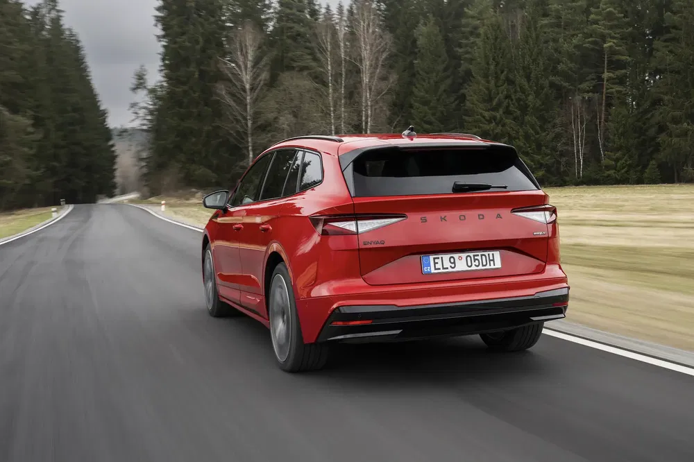 Škoda Enyaq iV rouge sur route bordée de forêts, arrière montrant la plaque d'immatriculation.