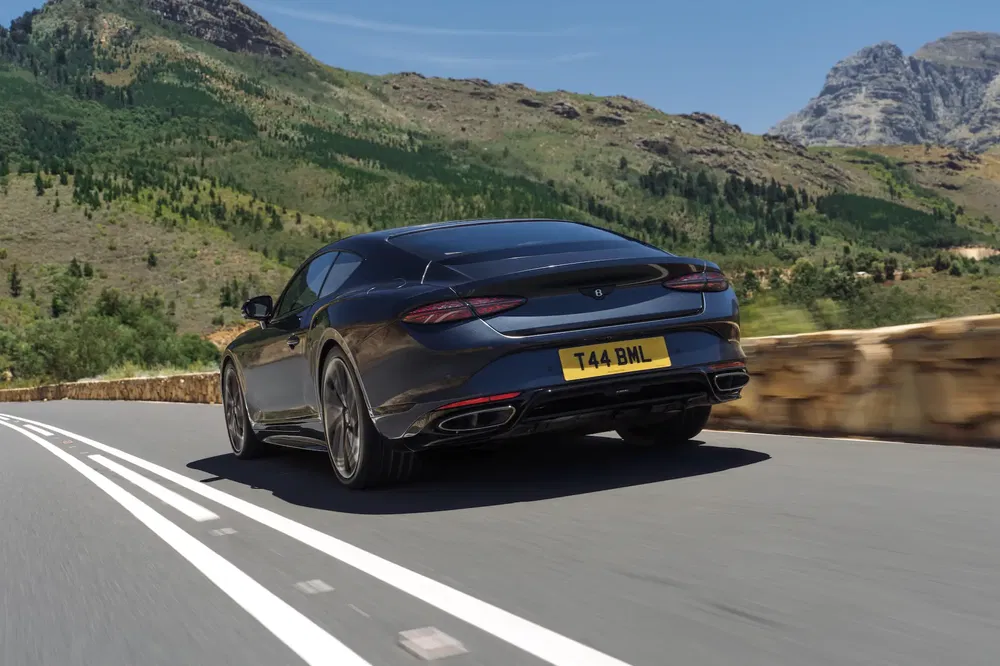 Bentley Continental GT noir roulant sur une route de montagne panoramique.
