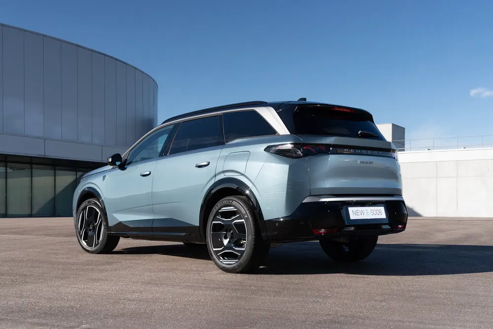 Achteraanzicht van de elektrische Peugeot E-5008 SUV, geparkeerd voor een modern gebouw.