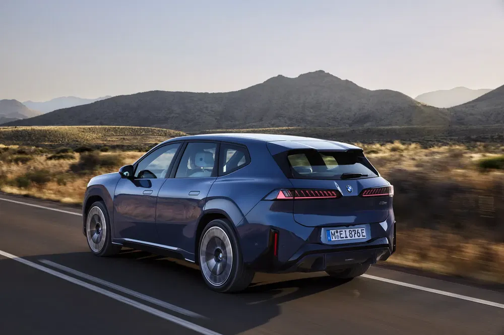 De blauwe BMW iX rijdt op een snelweg omringd door bergen in de schemering.