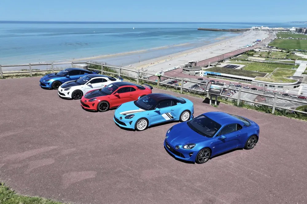 Collection de voitures Alpine A110 alignées sur un belvédère avec vue sur la mer.