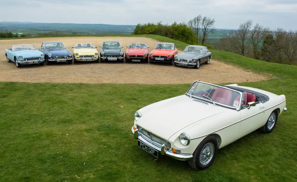 Collection de voitures classiques MG MGB décapotables sur une colline panoramique.