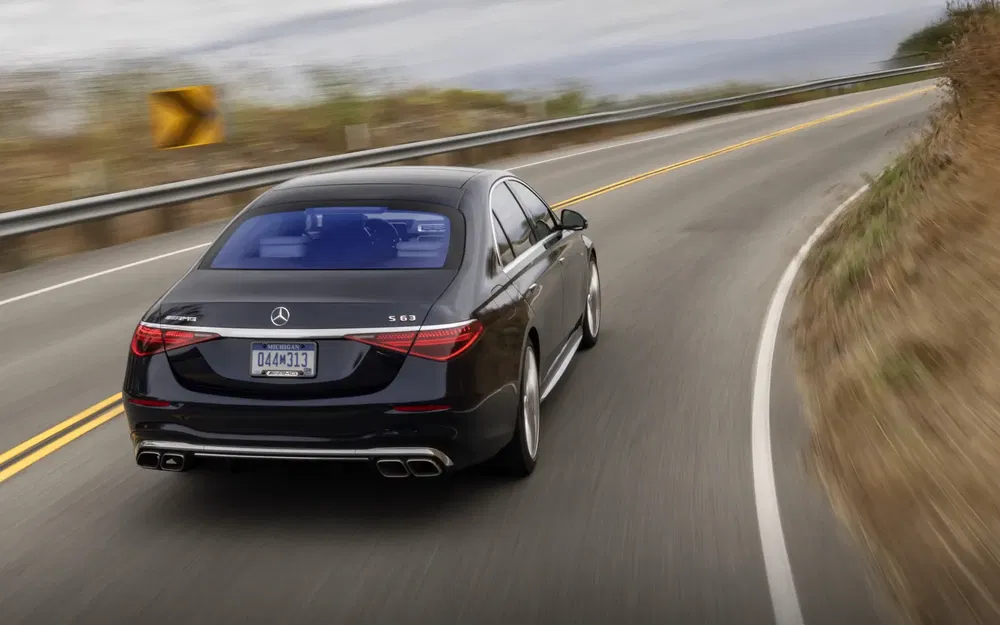 Mercedes-AMG S63 noire en virage sur route de campagne, dynamique et élégante.