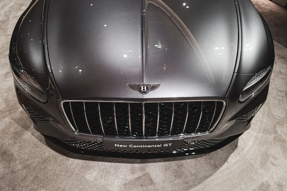 Vue avant de la Bentley Continental GT grise avec emblème distinctif, exposée sur tapis.