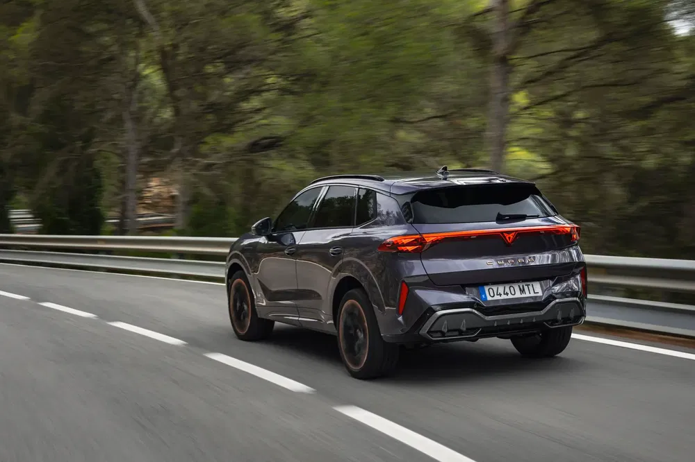 Cupra SUV rijdt snel op kronkelige weg omringd door groen bos.