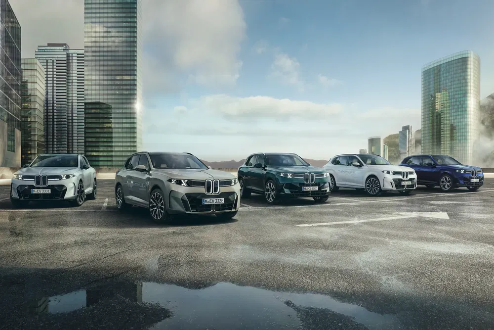Gamme de modèles BMW iX SUV alignés devant des gratte-ciel modernes, sous un ciel ensoleillé.