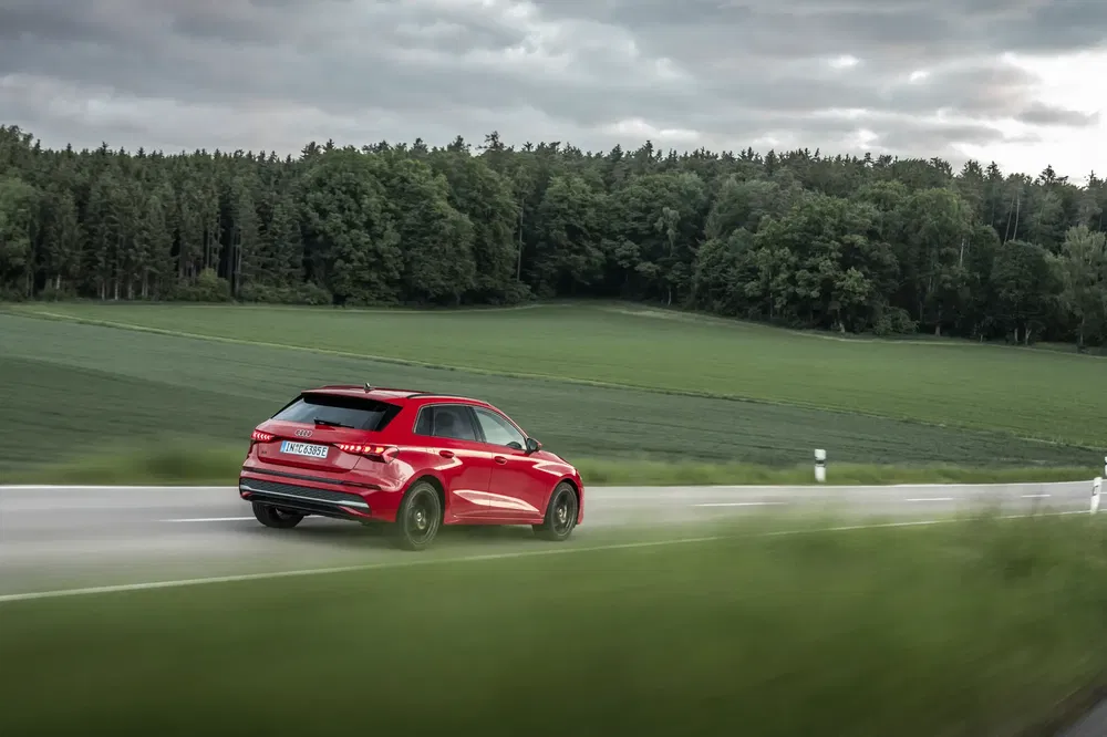 Audi Q3 rouge roulant sur une route de campagne entourée de prairies verdoyantes.