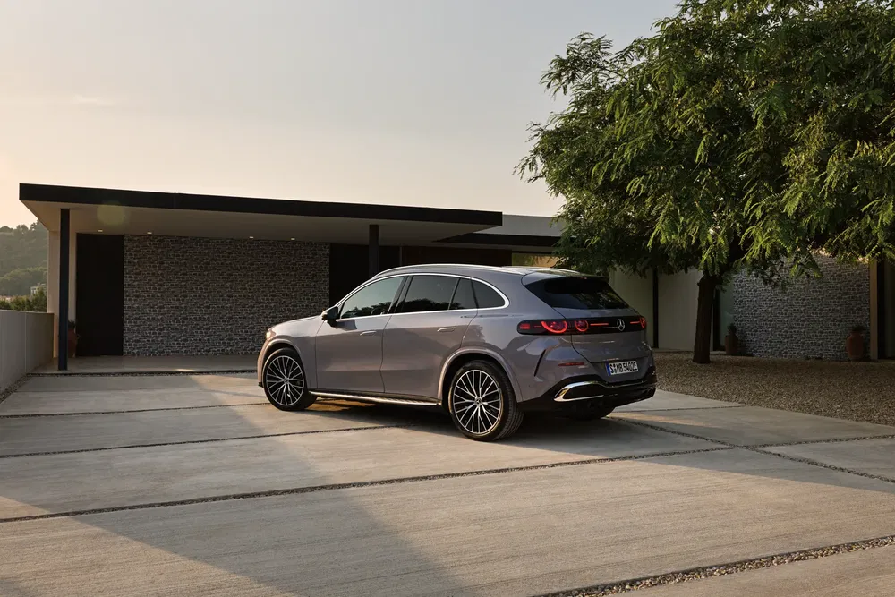 Grijze Mercedes-Benz EQC geparkeerd voor een moderne woning met omliggend groen.