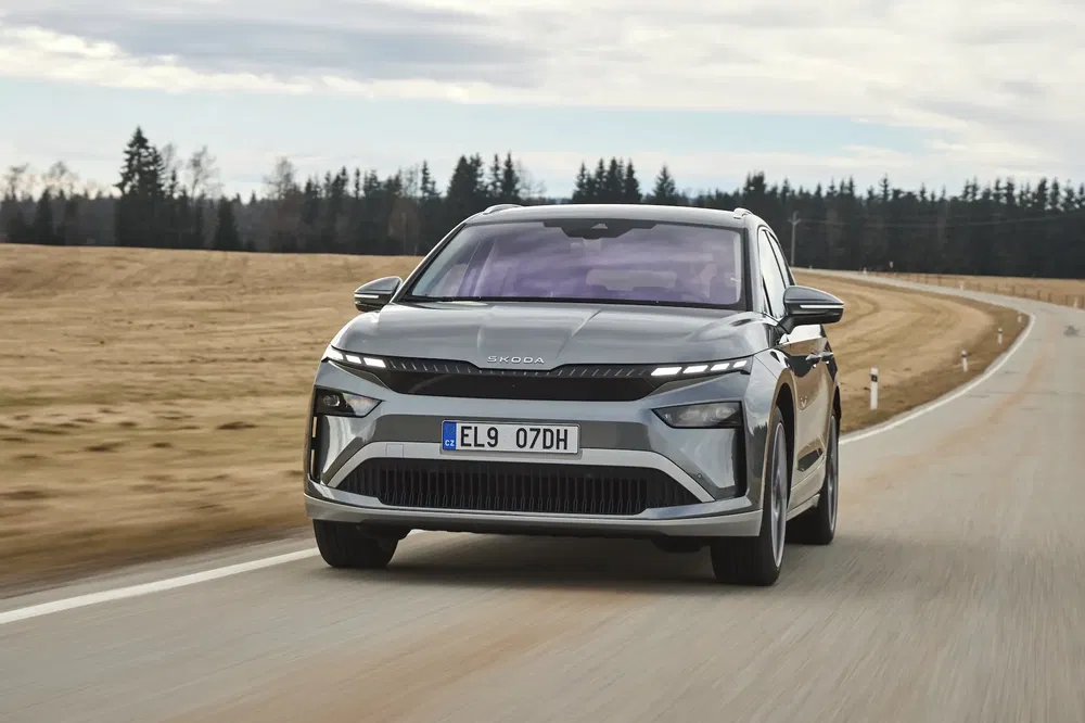 Skoda Enyaq, SUV électrique, roulant sur route de campagne boisée, sous ciel nuageux.