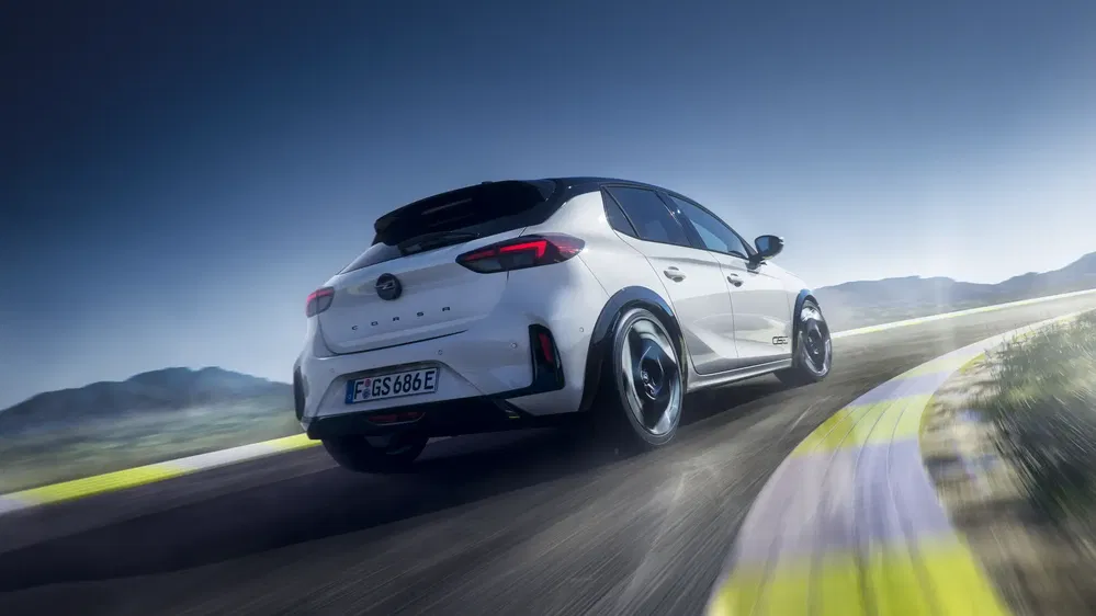 Opel Corsa blanche roulant sur une piste sinueuse, arrière plan montagneux.