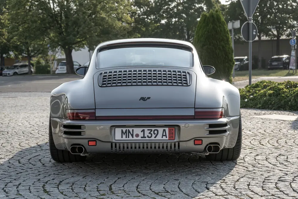 Zilveren RUF-auto op geplaveide weg, achteraanzicht met opvallende achterlichten.