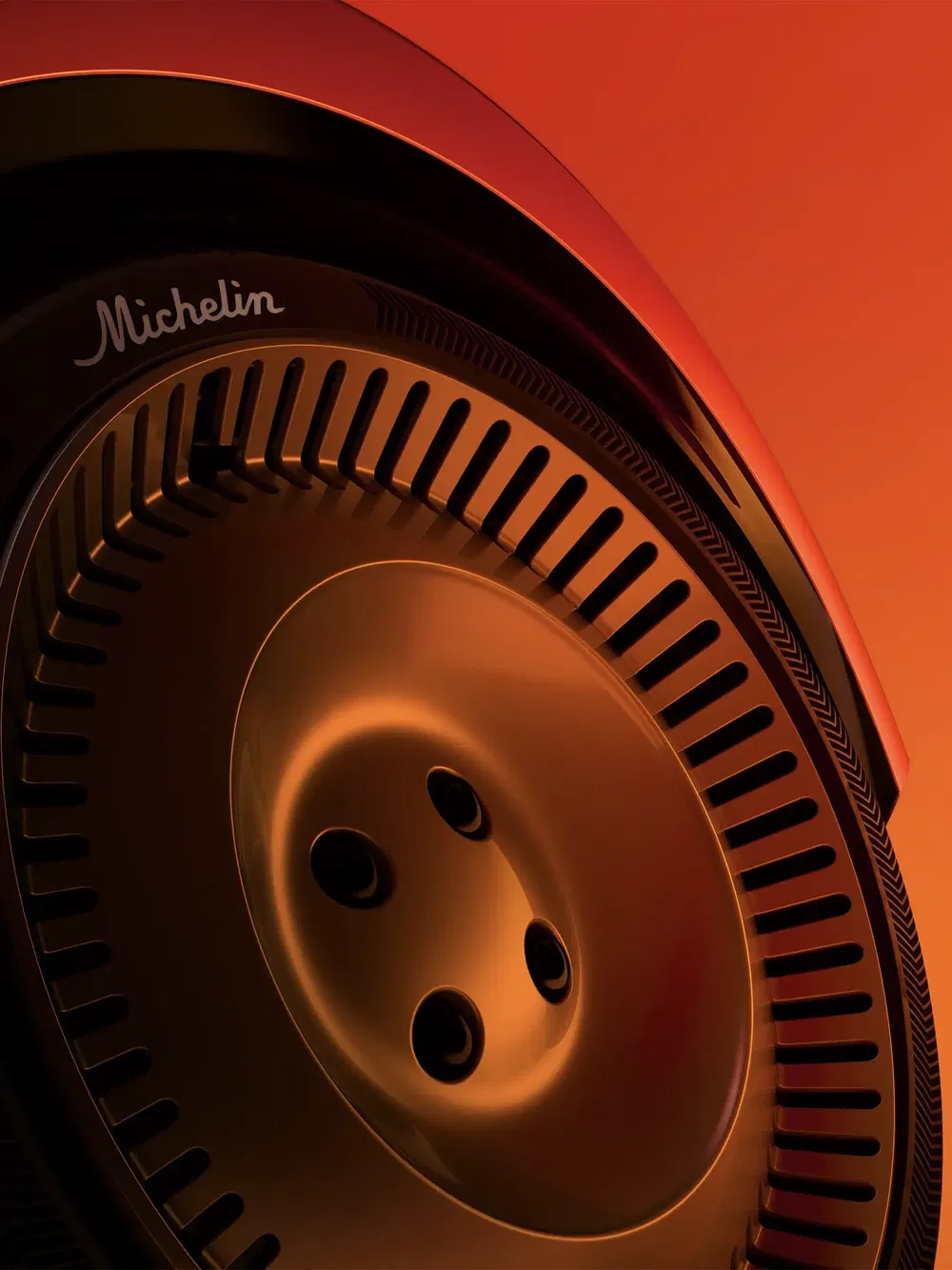 Gros plan d'un pneu Michelin avec jante futuriste sur fond orange vibrant.