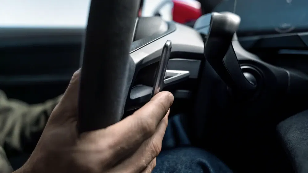 Main tenant un smartphone au volant en conduisant, geste de distraction potentielle.