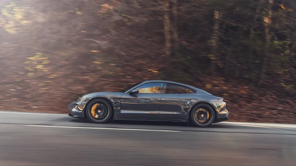 Voiture Porsche Taycan roulant sur une route entourée d'arbres en automne.