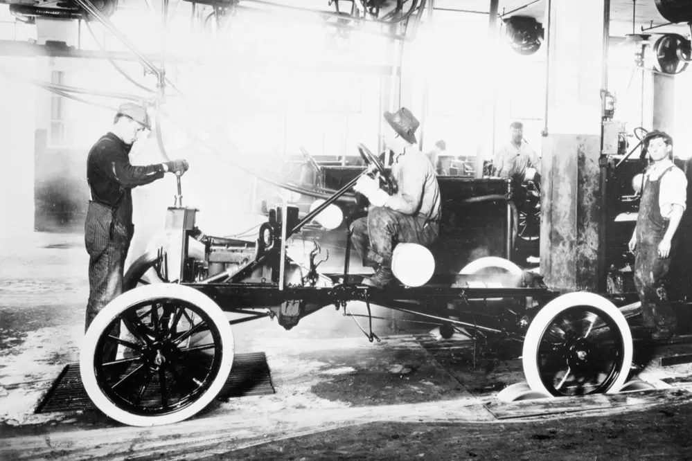 Ouvriers assemblant une Ford Model T dans une usine, processus de fabrication automobile des années 1900.