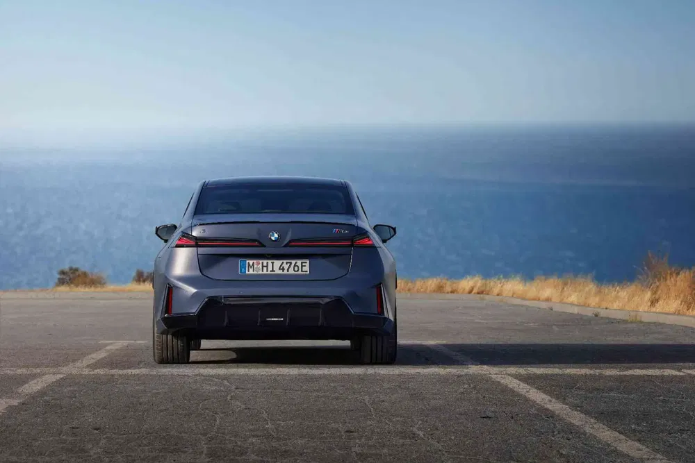 Vue arrière d'une BMW i7 garée en bord de mer, ciel bleu dégagé en arrière-plan.