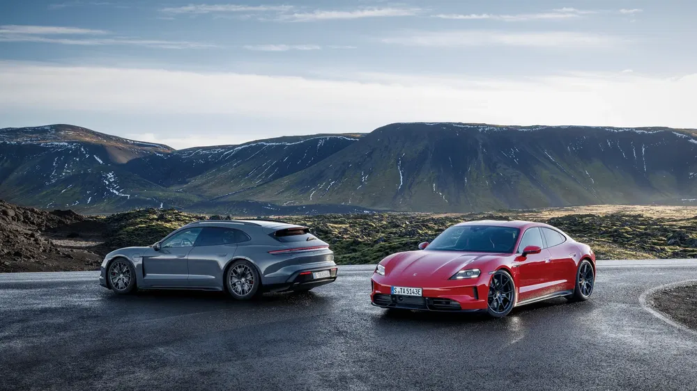 Deux Porsche Taycan sur route de montagne avec paysage de fond spectaculaire.
