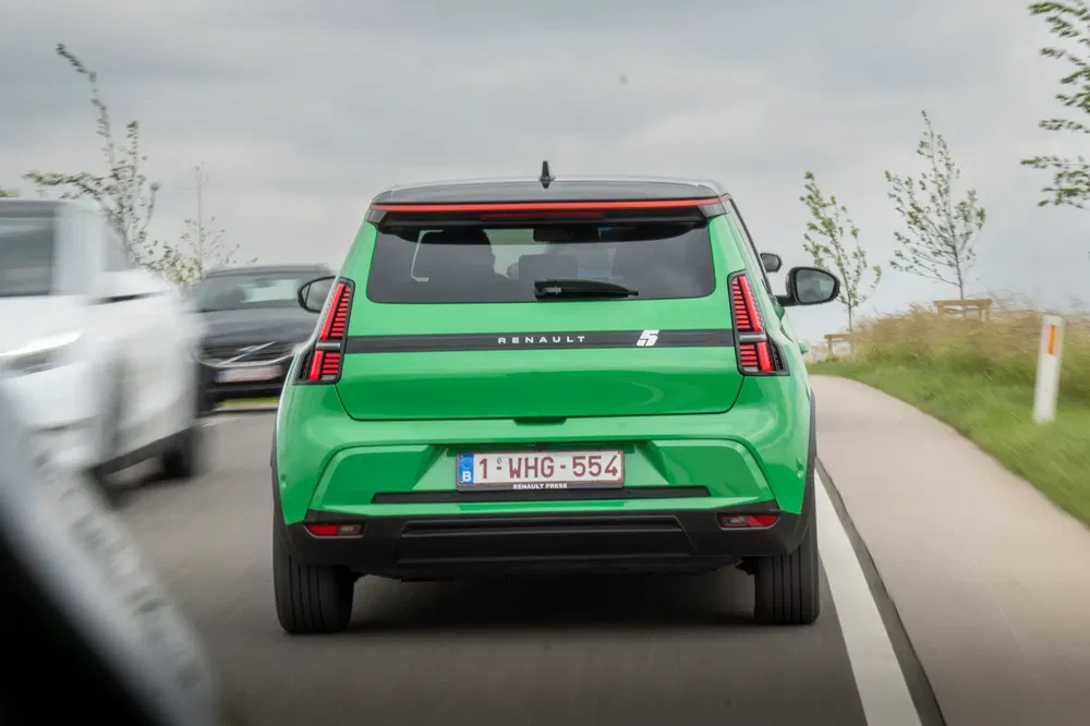 Renault 5 verte sur une route, plaque belge visible, voitures en mouvement autour.
