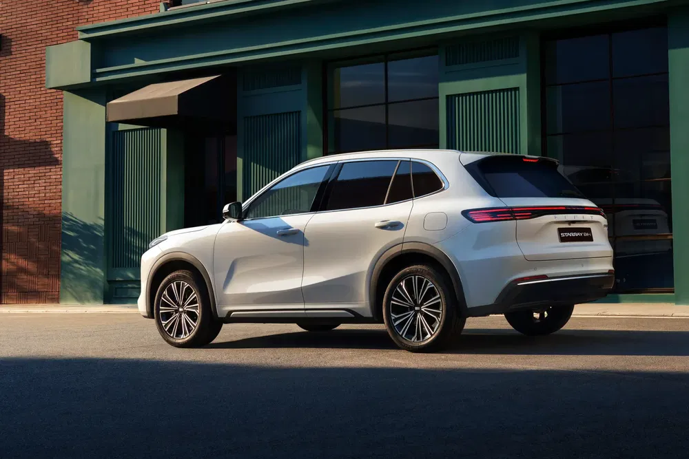 Zilveren elektrische Mercedes EQE SUV voor een zonnig gebouw met groene en bakstenen muren.