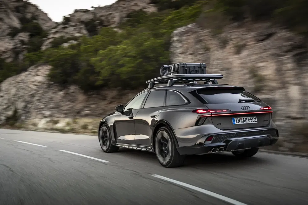 Grijze Audi A6 Allroad met dakdrager, rijdend op bergweg.